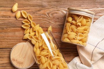 Jars with raw conchiglie pasta on wooden background