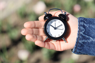 Female hand with small alarm clock outdoors, closeup