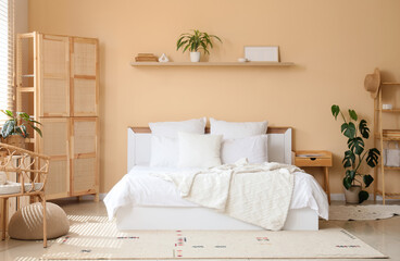 Interior of cozy bedroom with wooden folding screen, shelf and plants
