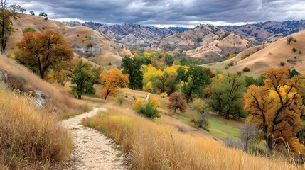 A winding dirt path meanders through a vibrant autumnal landscape, dotted with colorful trees and rolling hills under a dramatic sky.