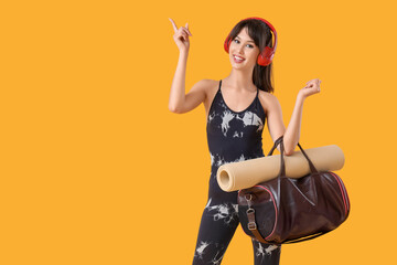 Obraz premium Young woman in headphones with sports bag pointing at something on yellow background