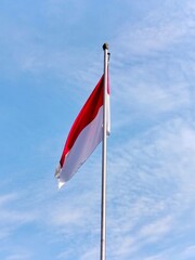 Fototapeta premium The Indonesian flag on a large pole against a blue sky, waving the red and white flag.