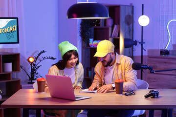 Young podcasters with notebook at table in recording studio