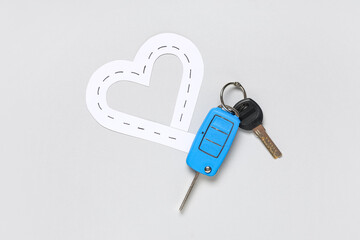 Car keys with paper road in shape of heart on light background