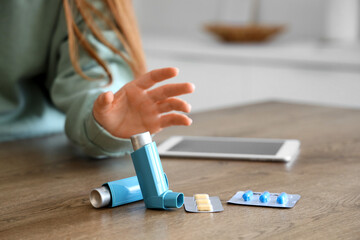 Woman taking inhaler from table with pills and tablet computer in kitchen