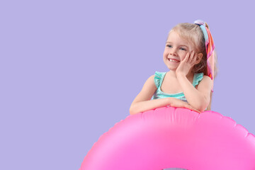 Cute little happy girl in swimsuit with pink inflatable ring on purple background