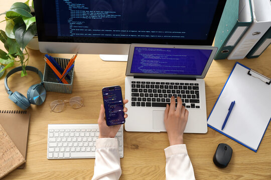 Female programmer's hands working with laptop and mobile phone on table in office, top view