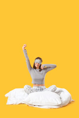Fototapeta premium Young woman in pajamas sitting on blanket against yellow background