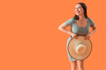 Stylish young woman with summer hat on orange background
