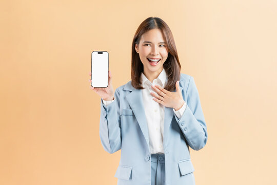 Confident Asian businesswoman holding smartphone mockup of blank screen and smiling on beige color background.