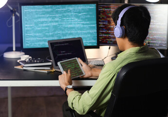 Male programmer working with tablet computer in office at night, back view