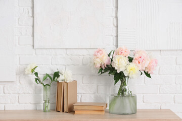 Vases with bouquet of beautiful peonies and books on table near white wall, closeup
