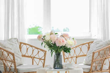 Vase with bouquet of beautiful peonies and cup of tea on table in stylish room, closeup