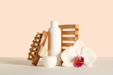 Anti-cellulite massage brush with cosmetic products and orchid flower on table near beige wall
