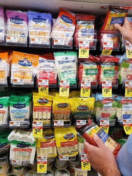 Wilmington, Delaware, U.S - Aug 19, 2025 - A shopper choosing packages on shelves, filled with various brands and types of string cheese and cheddar blocks