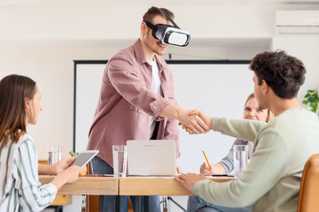 Young man in VR glasses with his colleague shaking hands at office
