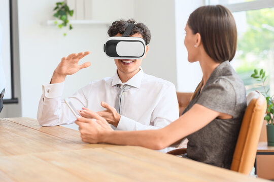 Young businessman using VR glasses with his colleague at table in office