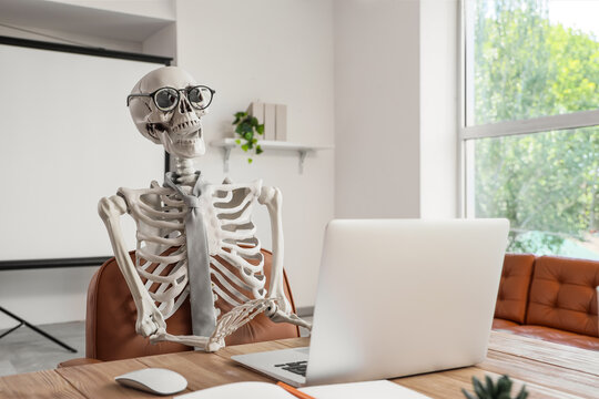 Human skeleton model with laptop at desk in office