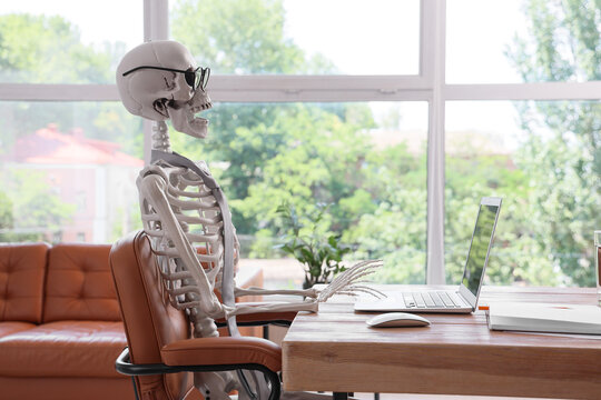 Human skeleton model with laptop at desk in office