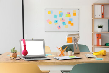 Table with blank laptop, headphones and sticky notes prepared for business meeting in conference hall