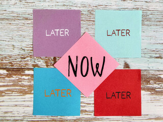 Stop procrastination concept with words of later and now on notepaper background. Stock photo.