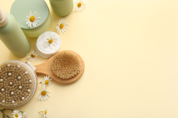 Composition with chamomile flowers, massage body brushes, jar and bottles of cosmetic products on beige background, closeup