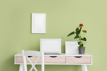 Beautiful Anthurium flower and blank laptop on desk near green wall in office