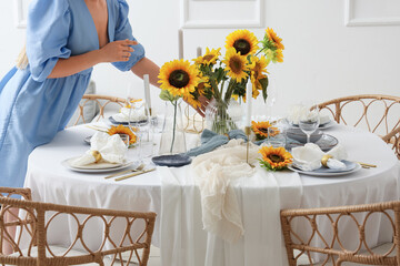 Young woman decorating served dining table with beautiful sunflowers