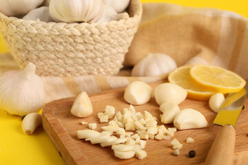 Wooden board with fresh garlic cloves and slices of lemon on yellow background