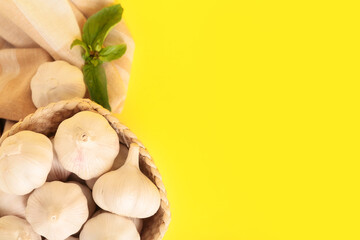 Wicker basket with fresh garlics and basil leaves on yellow background