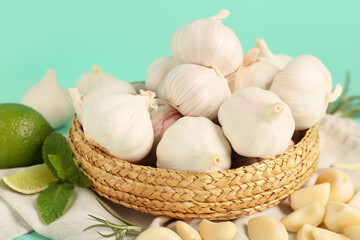 Wicker bowl with fresh garlics, mint and lime on turquoise background