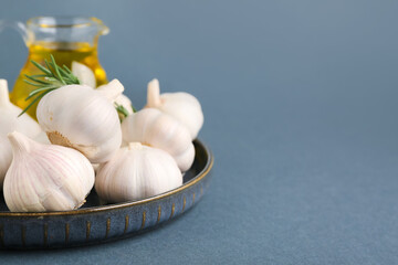 Plate with fresh garlics, rosemary and jug of oil on grey background