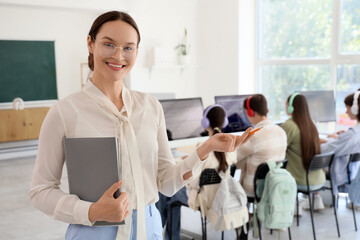Female teacher with notebook against teenage students studying at school computer lab