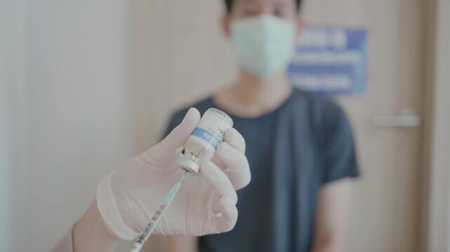 A man is holding a vaccine bottle and wearing a mask. The bottle is labeled with the word "COVAX" and the man is wearing a blue shirt