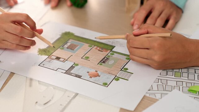 Professional engineer team discussion about house design on meeting table with architectural equipment and building blueprint scatter around at modern office. Focus on hand. Closeup. Delineation.