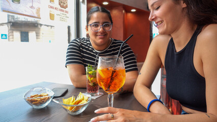 Two young women enjoying refreshing aperitif cocktails and snacks on a sunny afternoon at a cafe table outside on a warm day