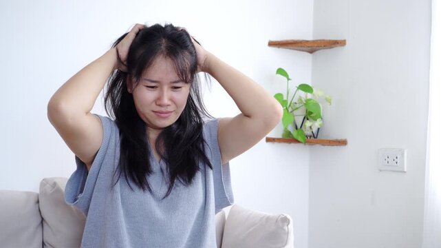 Unhappy Asian woman scratching her scalp and feeling discomfort from dandruff, itchy hair, and hair loss problem, suffering from seborrhea, dry scalp, and hair care troubles 
