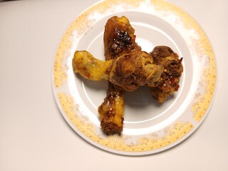 Ayam Kecap, or chicken cooked with sweet soy sauce. One chicken drumstick on white plate,