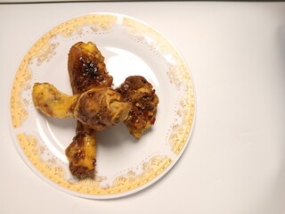 Ayam Kecap, or chicken cooked with sweet soy sauce. One chicken drumstick on white plate,