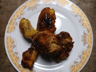 Ayam Kecap, or chicken cooked with sweet soy sauce. One chicken drumstick on white plate,