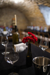 Stone cellar dining hall with long tables, wine glasses, candles, and red flowers creating a rustic romantic atmosphere