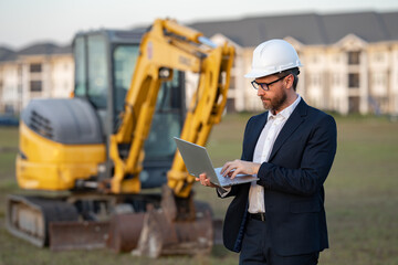 Architect at a construction site. Architect man in helmet and suit at modern home building construction. Architect with a safety vest and suit. Confident architect standing at house background.