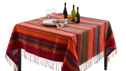 Colorful fringed tablecloth with striped pattern set for dinner with wine bottles, glasses, and elegant tableware on a square wooden table