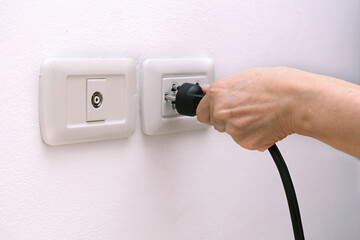 Hand holding plug to connect a power plug into a electric outlet on a wall.