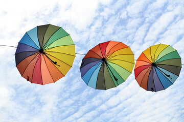 Colorful umbrella hanging on a wire against a bright blue sky