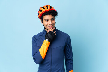 Venezuelan cyclist man isolated on blue background looking up while smiling