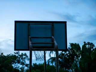 Basketball Hoop and Net Against Blue Sky with Green Trees - Outdoor Sport Court in Twilight.