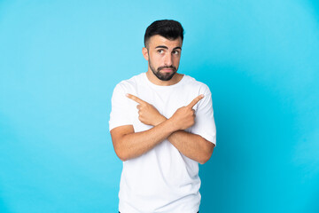 Fototapeta premium Caucasian man over isolated blue background pointing to the laterals having doubts