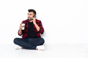 Young handsome man sitting on the floor holding coffee to take away and a mobile