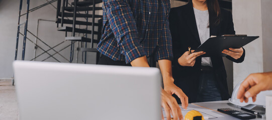 Construction manager and engineer dressed in orange work vests and hard helmets explore construction documentation on the building site near the steel frames